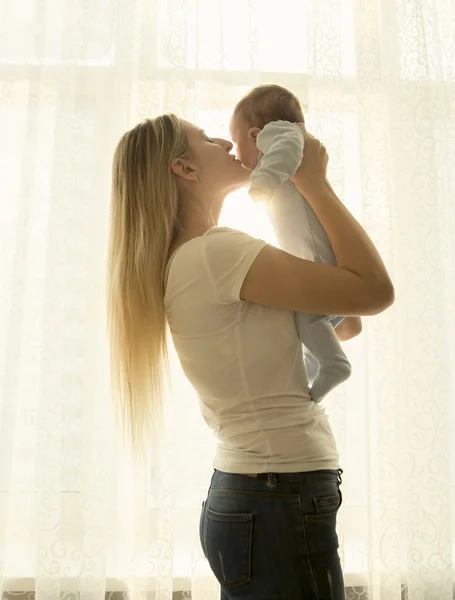 Portrait of mother holding her little baby at window — Stock Photo, Image