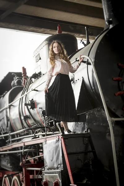 Beautiful woman in long skirt posing on old steam train — Stock Photo, Image