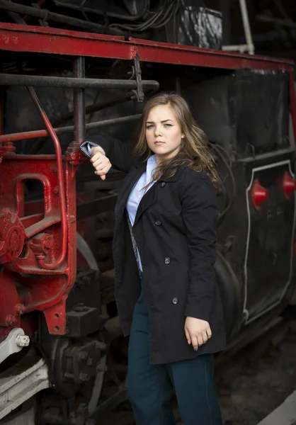 Beautiful young woman posing at big steam locomotive — Stock Photo, Image