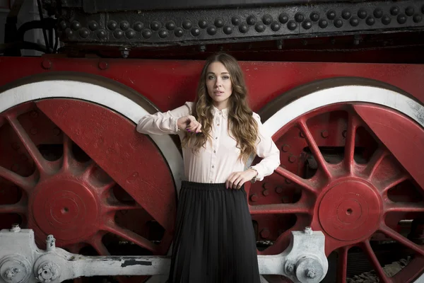 Portrait of beautiful woman leaning on big red wheel of old trai — Stock Photo, Image