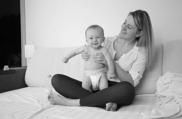 Black and white shot of mother sitting on bed with her baby boy — Stock Photo, Image