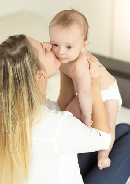 Feliz joven madre sosteniendo a su hijo bebé y besándolo en la mejilla — Foto de Stock