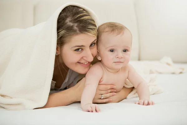 Porträt einer glücklichen jungen Mutter, die mit ihrem kleinen Sohn unter der Decke liegt — Stockfoto