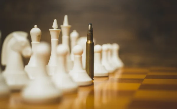 Closeup photo of bullet in row of white chess pieces on wooden b — Stock Photo, Image