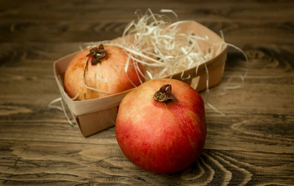 Closeup of two pomegranates lying in basket on old wooden desk — Stock Photo, Image