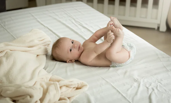 Söt baby liggande på sängen och hålla fötterna — Stockfoto