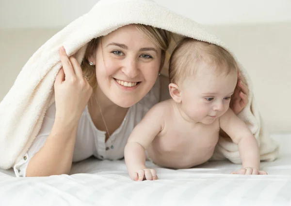 Retrato de la madre sonriente y el bebé cubriendo con manta en la cama — Foto de Stock