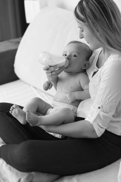 Black and white shot of beautiful mother feeding her baby on bed — Stock Photo, Image