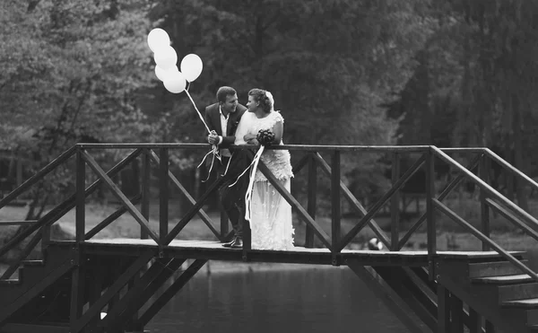 Black and white photo of newlyweds standing on bridge across riv — Stock Photo, Image