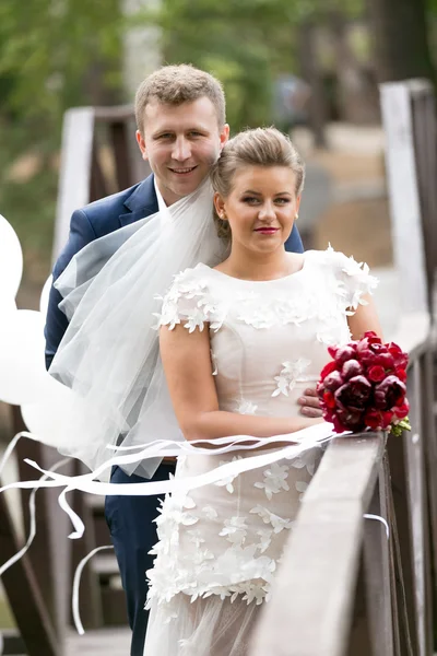 Happy bride and groom on wooden bridge at windy day — Stock Photo, Image