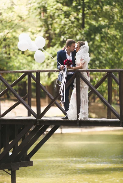 Glückliche Frischvermählte posieren auf Holzbrücke mit Luftballons — Stockfoto