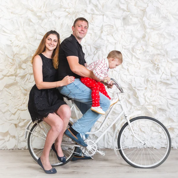 Happy family with baby boy posing on retro bicycle at studio — Stock Photo, Image