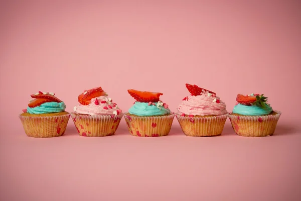 Wiersz, różowy i niebieski Cupcakes z świeże truskawki, na plecach różowe — Zdjęcie stockowe