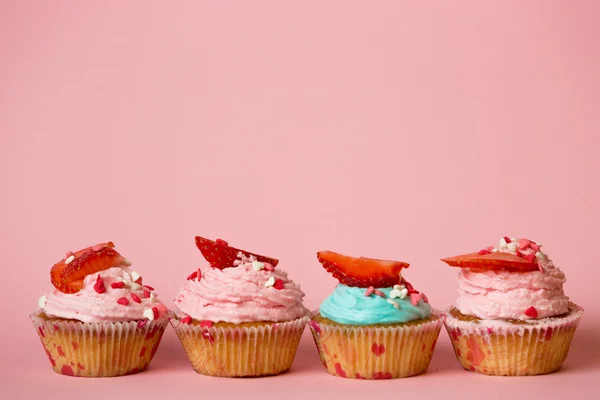 Cupcakes rosados y azules con espolvoreos y fresas sobre rosa b — Foto de Stock