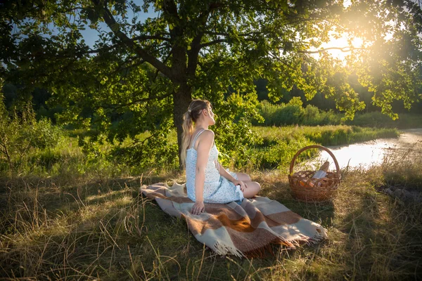 Schöne Frau sitzt unter einem großen Baum auf dem Feld und betrachtet s — Stockfoto