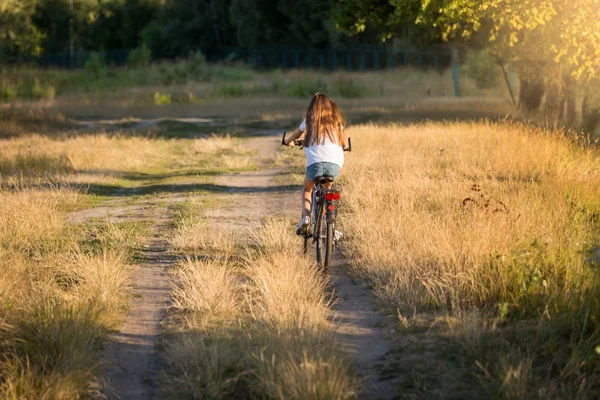 Kobieta jazdy na rowerze na polnej drodze w łące — Zdjęcie stockowe