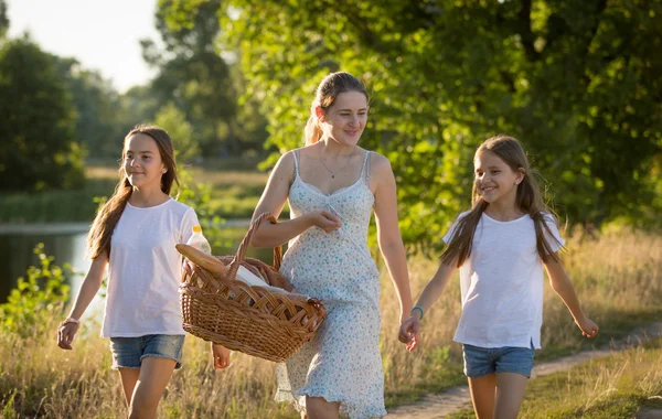 Feliz madre con dos hijas caminando por el río en el prado en — Foto de Stock