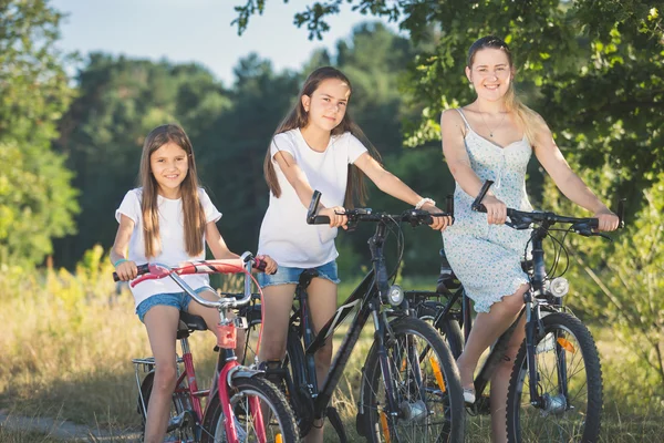 Portrét dvou sesterských Cyklistika s matkou na louce u jezera — Stock fotografie