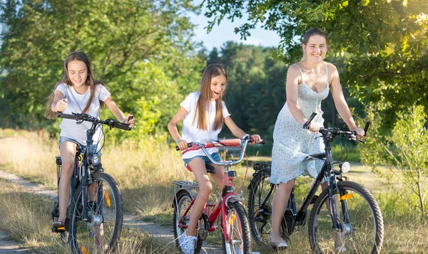 Hermosa madre ciclismo con dos hijas en el prado — Foto de Stock