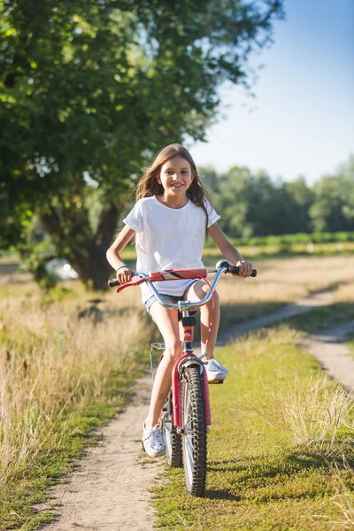 Веселая девушка с длинными волосами верхом на велосипеде по грунтовой дороге в — стоковое фото