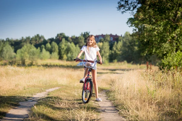 Chica alegre montar en bicicleta en el prado en el día soleado — Foto de Stock