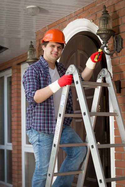 Lachende werknemers in veiligheidshelm reparatie buiten lamp in huis — Stockfoto