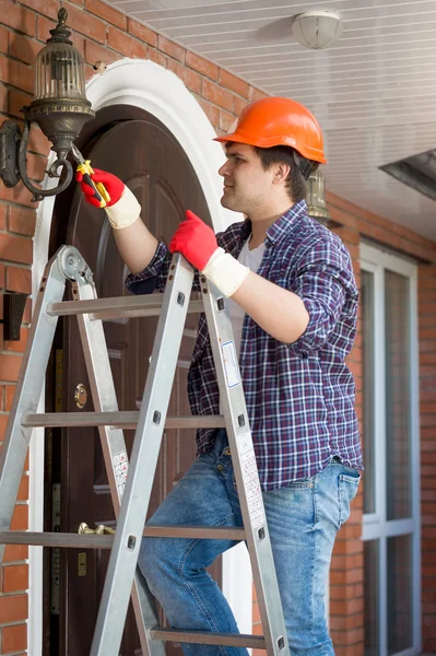 Elektricien in veiligheidshelm staande trapladder en herstel lamp op — Stockfoto