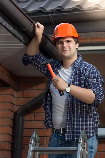 Trabajador guapo en hardhat posando con martillo en escalera —  Fotos de Stock