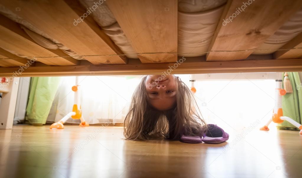 Beautiful smiling teenage girl looking under the bed for slipper