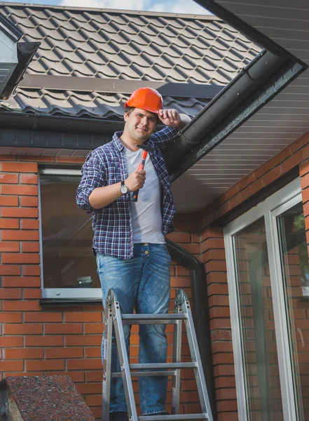 Glimlachend timmerman poseren met de hamer op stap ladder onder de ro — Stockfoto