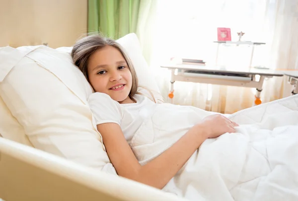 Retrato de menina sorridente deitada na cama na manhã ensolarada — Fotografia de Stock