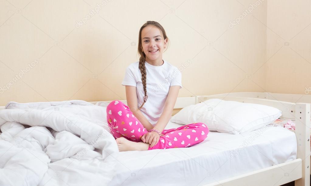 Teenage girl in pink pajamas sitting on bed with white sheets an