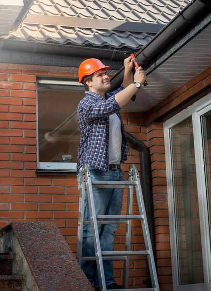 Worker standing on step ladder and repairing gutter on house — Stock Photo, Image