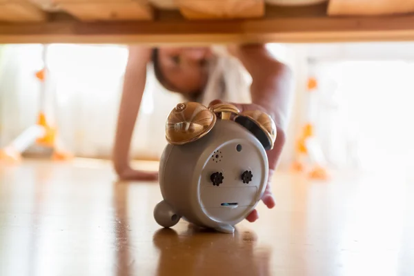 Closeup of beautiful girl reaching for alarm clock under the bed — Stock Photo, Image