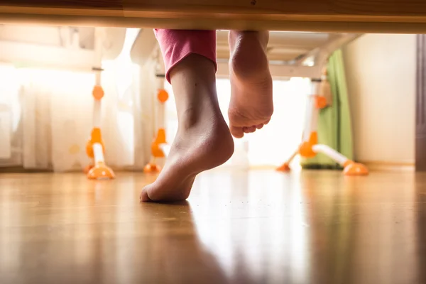 Fechar os pés femininos sob a cama no chão de madeira — Fotografia de Stock