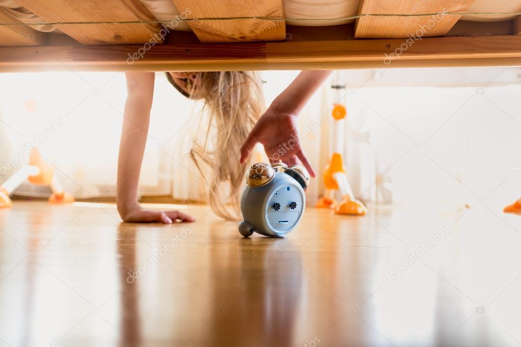 Toned photo of annoyed girl reaching for alarm clock under the b