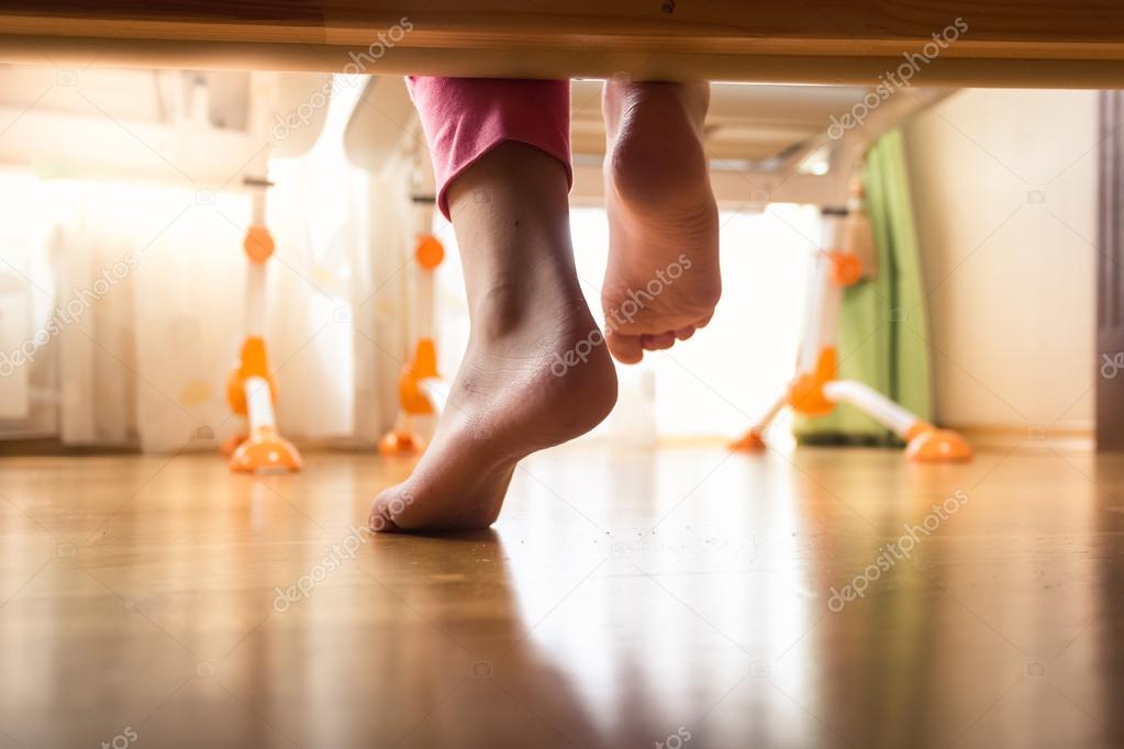 Closeup of female feet under the bed on wooden floor