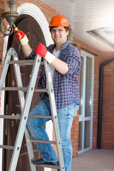 Lachende elektricien permanent op trapladder en repareren van buiten — Stockfoto