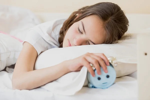 Cute teenage girl holding alarm clock under pillow — Stock Photo, Image