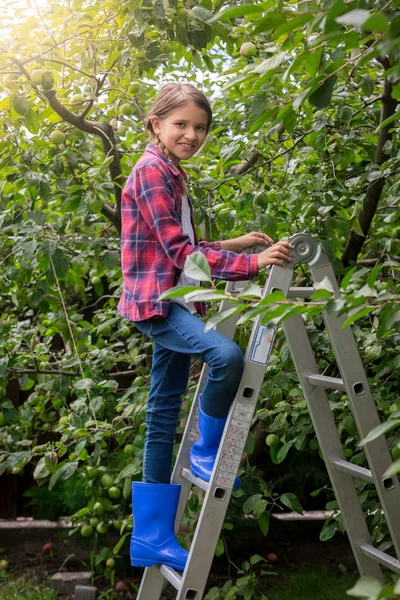 Smiling girl in checkered shirt climbing up the stepladder at or — Stock Photo, Image
