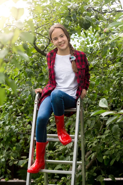 Девочка-подросток в красных резиновых сапогах позирует на лестнице в яблоневом саду — стоковое фото