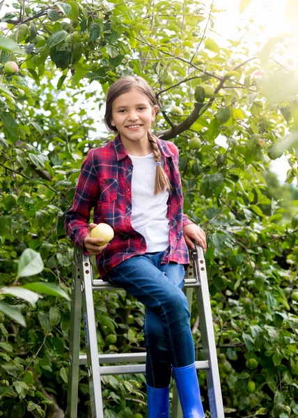 Smiling teenage girl sitting on stepladder at apple garden — Stock Photo, Image