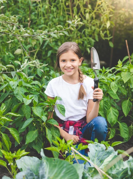 Schattige lachende meisje poseren met de troffel in de bloeiende tuin — Stockfoto