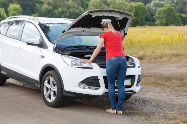 Woman looking under the hood of broken car at offroad — Stock Photo, Image