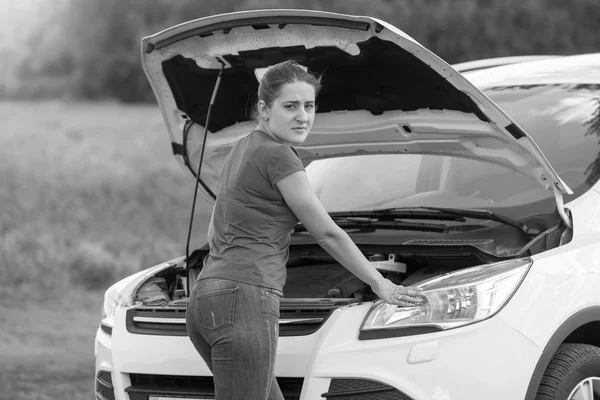 Black and white portrait of woman standing at broken car with op — Stock Photo, Image