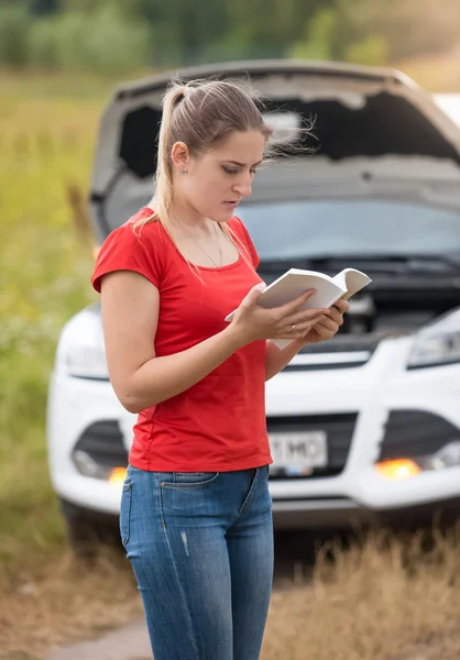 Retrato de mulher lendo manual do proprietário em carro quebrado no prado — Fotografia de Stock