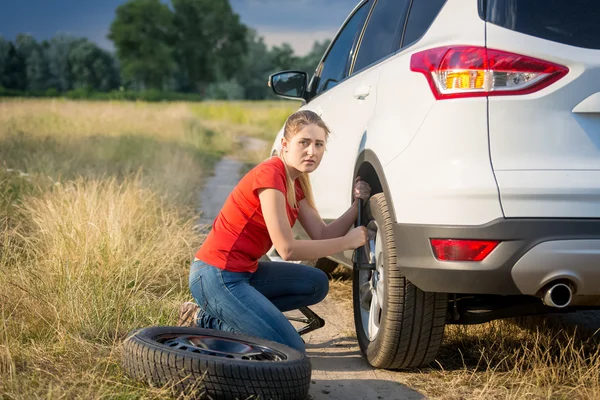 Bella donna che cambia ruota auto sulla strada rurale andando throu — Foto Stock