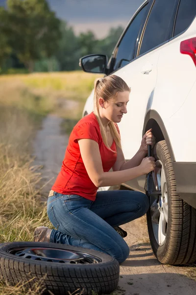 Hermosa mujer cambiando neumático pinchado en el camino rural — Foto de Stock