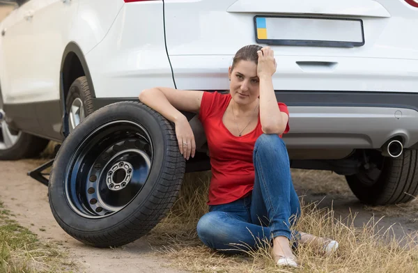 Mujer molesta sentada en el suelo junto al neumático de repuesto — Foto de Stock