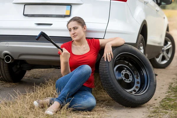 Mujer frustrada sentada junto a un coche roto y tratando de cambiar —  Fotos de Stock